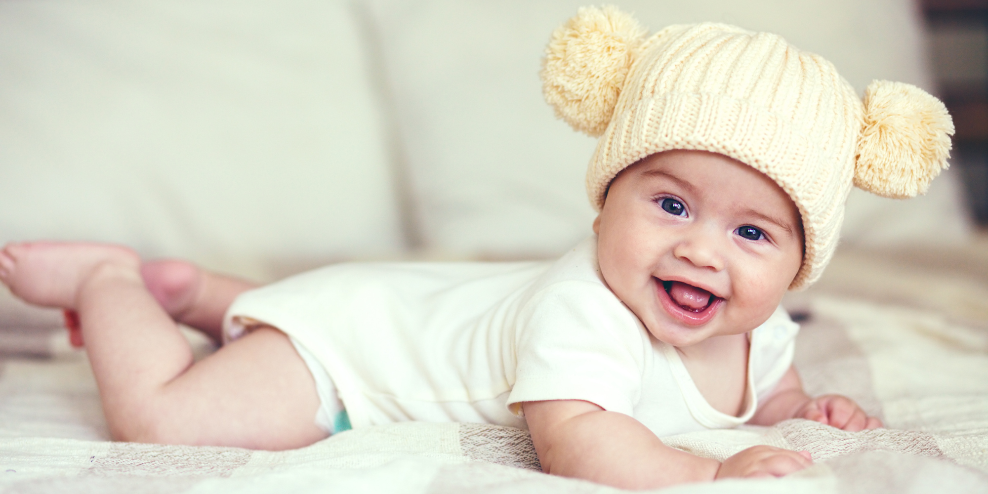 Baby wearing a cream-colored knit hat with two pom-poms on a light background