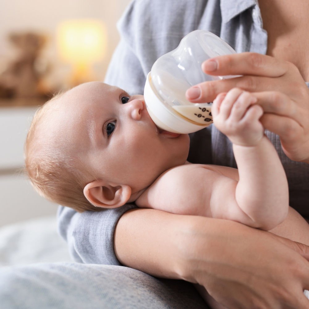 Baby being fed from a bottle by an adult in a cozy indoor setting

