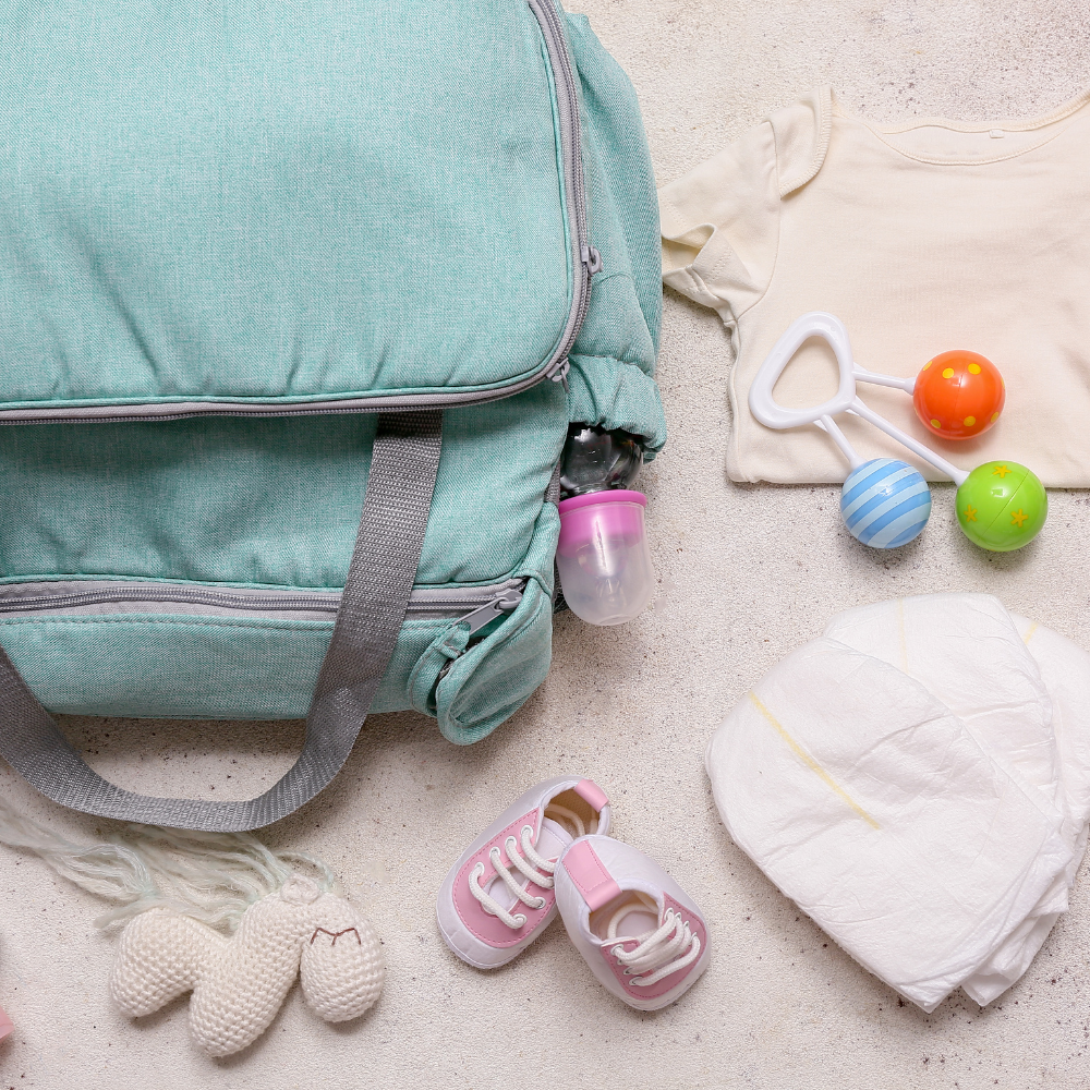 Mint green diaper bag with baby items including shoes, a hat, and toys on a light surface.

