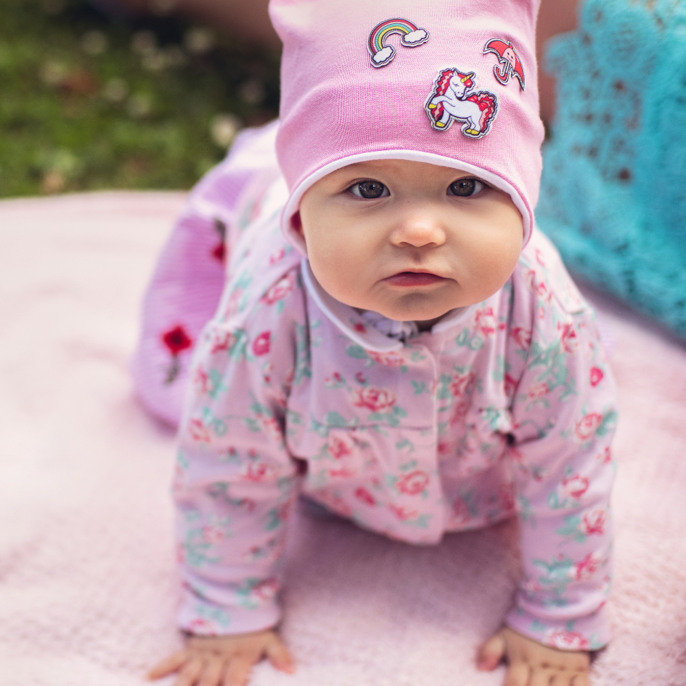 Baby in a pink floral outfit and unicorn hat outdoors

