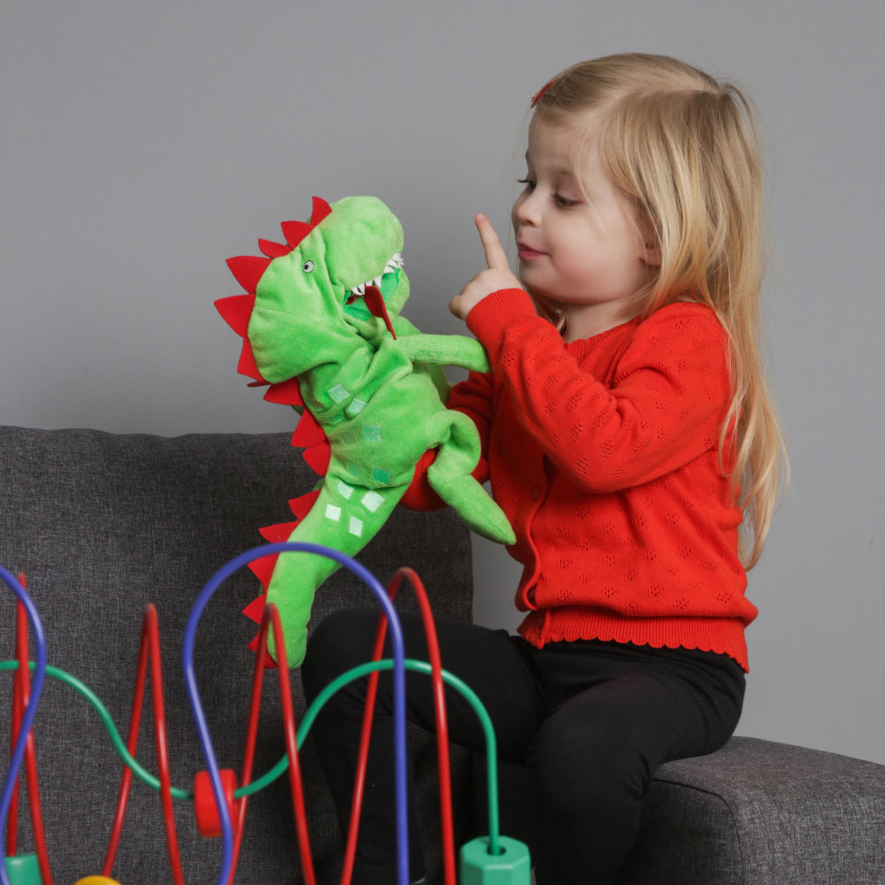 Child playing with a green dinosaur puppet on a gray background

