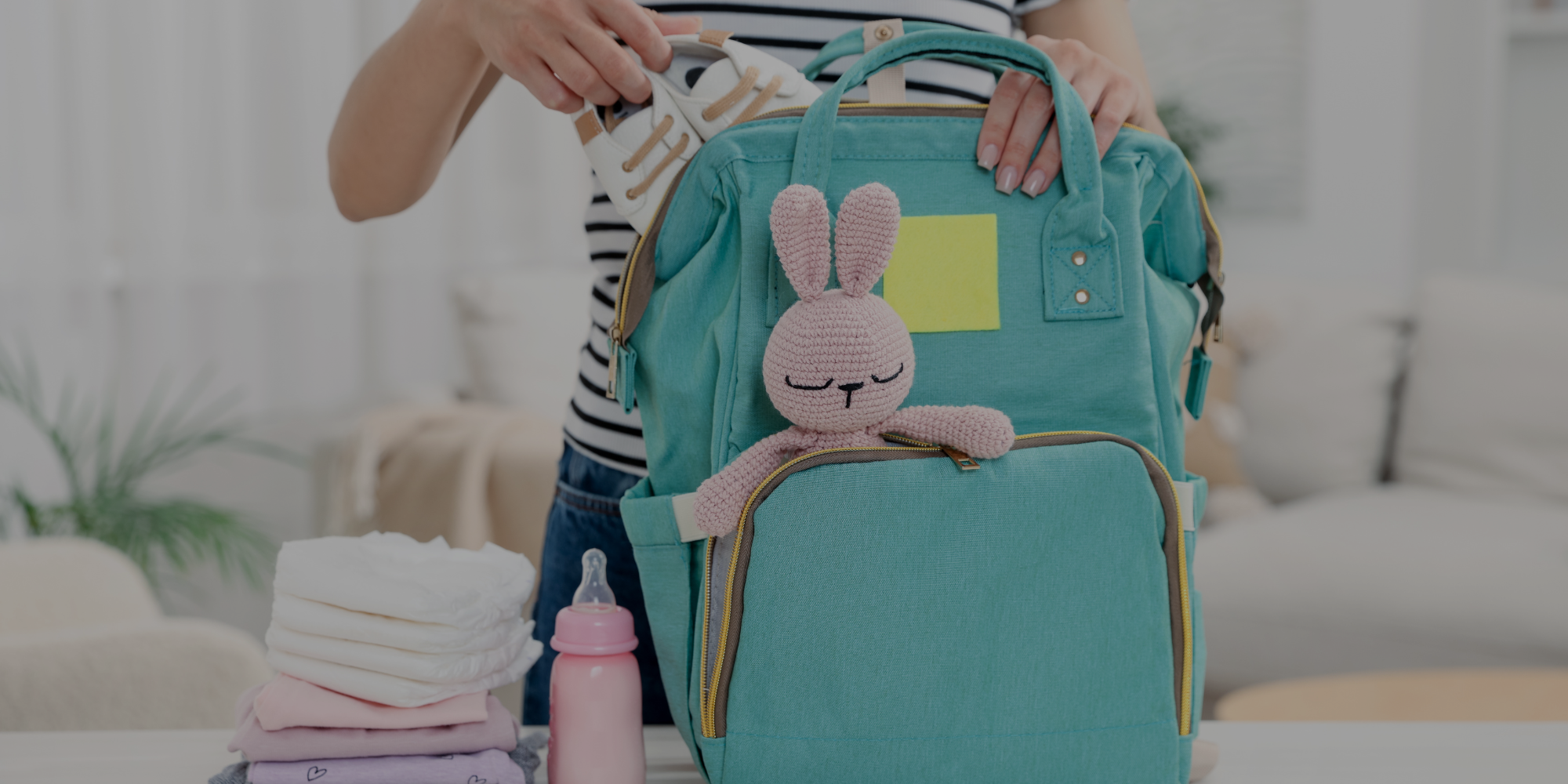 Teal diaper bag with a rabbit design held by a person in a living room.

