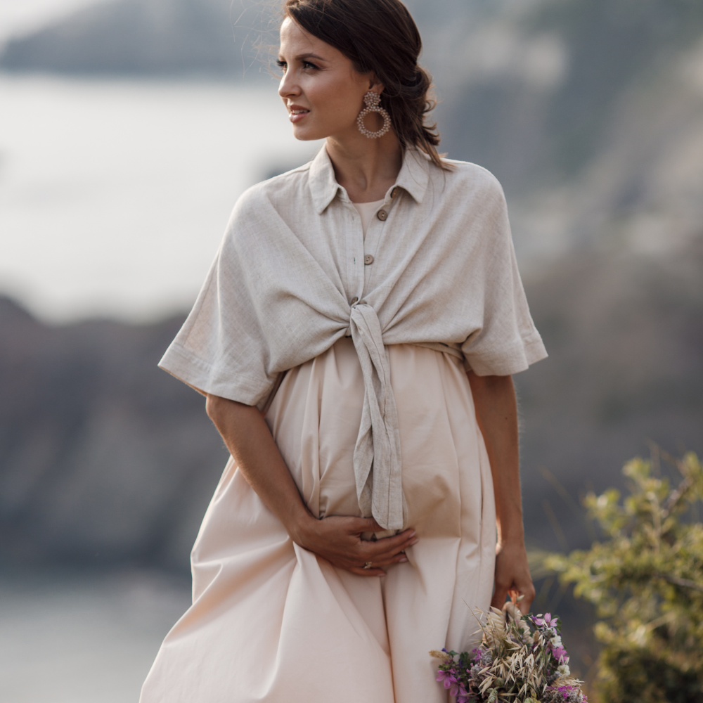 Woman in a light-colored outfit standing outdoors with mountains in the background

